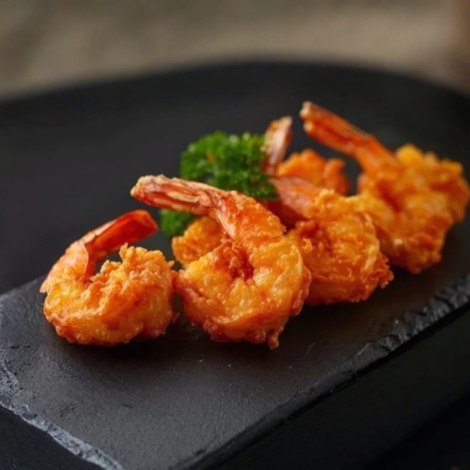 Golden-fried shrimp with tails on, garnished with parsley, served on a dark slate board.