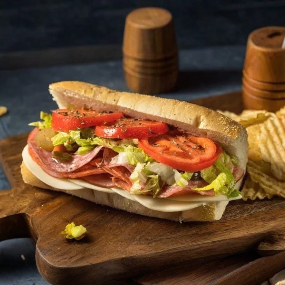A Ciro's Flying Pizza Italian sub sandwich with chips on a wooden board.