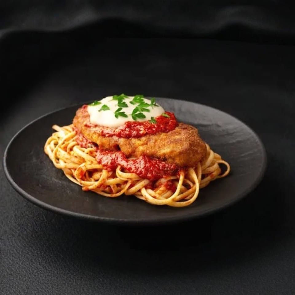 Chicken parmesan with linguine pasta, red sauce, and melted cheese, garnished with parsley.
